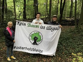 Susanne Herhaus, Till Sörensen-Siebel und Gerd-Peter Zielezinski, Ratsfraktion DIE LINKE Wuppertal, besuchen die Waldschützer*innen. Sie halten ein Transparent mit der Aufschrift: "Kein Baum ist illegal. #osterholzbleibt.